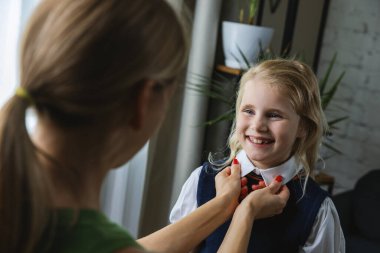 Anne, kızının ilk okul günü için evdeki oturma odasında hazırlanmasına yardım eder ve destek olur.