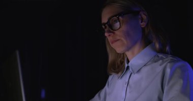 Şirket kadını gece geç saatlere kadar karanlık ofiste dizüstü bilgisayarda çalışıyor. aşırı çalışma ve işkolik konsept