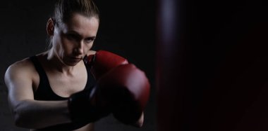 Eldivenlerle boks yapan kararlı bir kadın ve spor salonunda kum torbası. Güç, dayanıklılık ve koordinasyon eğitimi. Boşluğu kopyala