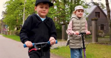 Çocuklar dışarıda scooter kullanıyor.