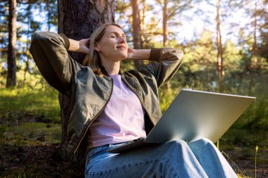 İşe ara vermiş, serbest çalışan bir kadın parkta dinleniyor ve uzaktan çalışırken doğanın tadını çıkarıyor. dijital göçebe yaşam biçimi