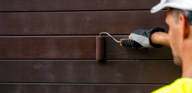 Boya silindirli boyacı, ahşap dış kaplamasını koruyucu renge boyuyor. Ahşap koruması. Kopyalama alanı olan pankart