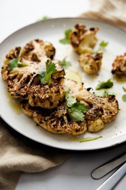 Baked cauliflower steak on white plate with cilantro leaves. High quality photo