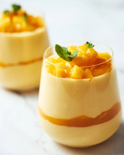 Mango mousse in glass. A delicate dessert of mango puree, cream, and condensed milk garnished with mint. Hand reaches for the glass with a spoon. High quality photo