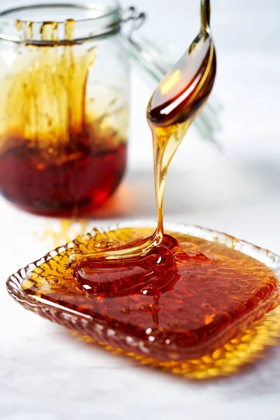Thick golden syrup or caramel or honey dripping from the spoon into the plate. White background. High quality photo