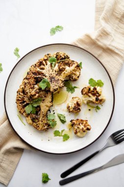 Baked cauliflower steak on white plate with cilantro leaves. High quality photo