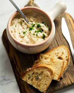 Sour cream, yogurt and caramelized onion spread dip in the bowl on wood board. bread pieces are near spreader with dip. High quality photo