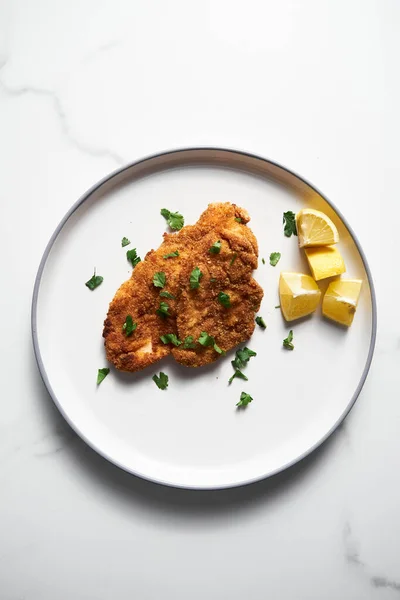 stock image Baked Chicken Schnitzel on white plate with lemon. Rack or grid with baked schnitzel in breadcrumbs on background. High quality photo