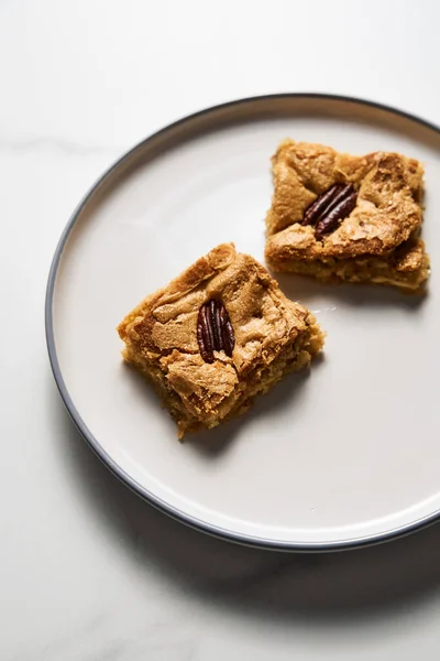 Two squares of Blondie cookies with pecan nuts on white plate. White chocolate sweet and tasty, chewy cookie bars. Close up. High quality photo