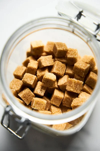 Brown sugar cubes in the jar on white marble background.. High quality photo
