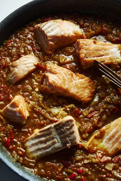 Frying pan with Indian salmon curry dish. Fried salmon fillets, stewed in curry sauce based on red tomatoes and other vegetables. Top view. High quality photo