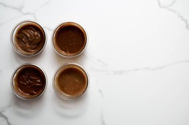 Beyaz mermer arka planda cam kaselerde dört farklı tuzlu karamel sosu. Tereyağı, kremalı ve tuzlu şeker. Yüksek kalite fotoğraf