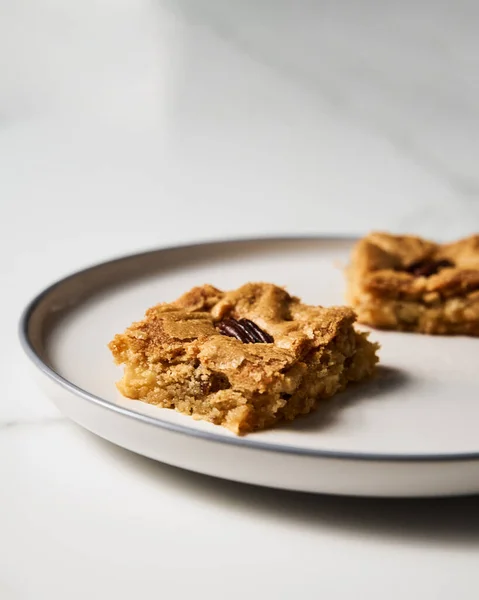 Two squares of Blondie cookies with pecan nuts on white plate. White chocolate sweet and tasty, chewy cookie bars. Close up. High quality photo