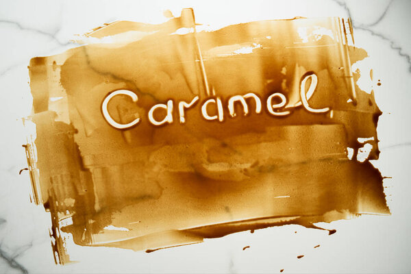 Salted Caramel sauce smeared on the tabletop with the Caramel word written on it with finger. A tabletop stained with caramel. Thin layer, copyspace. Top view food photo. High quality photo