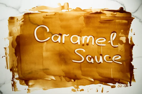 Salted Caramel sauce smeared on the tabletop with the Caramel sauce words written on it with finger. A tabletop stained with caramel. Thin layer, copyspace. Top view food photo. High quality photo