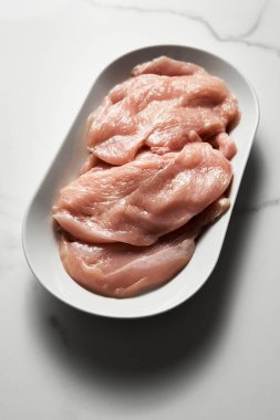 Çiğ tavuk filetosu beyaz mermer mutfak tezgahında oval bir tabakta şnitzel şeklinde kesilmiş. Yüksek kalite fotoğraf
