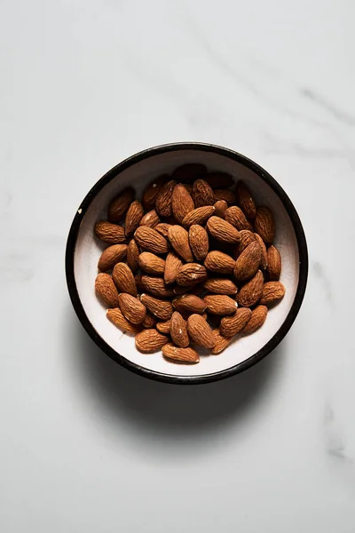 Roasted Almonds in the bowl on white marble kitchen countertop. Top view. High quality photo