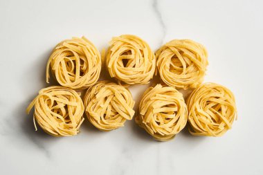 Beyaz mermer arka planda yuvalarda kuru tagliolini ya da tagliatelle makarna. Pişmemiş malzeme. Yüksek kalite fotoğraf