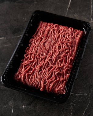 Dükkandan yeni alınmış taze ve çiğ kıymalı et konteynırı açıldı. Koyu mermer arka planda. Minimalist yemek fotoğrafı, sade. Yüksek kalite fotoğraf