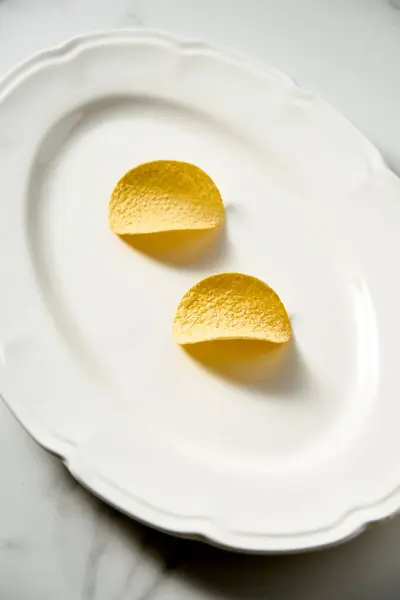 Two potato chips on white serving plate. White marble background. Minimalistic food photo. High quality photo