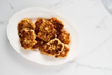 Beyaz tabak üzerinde mozzarella peynirli tavuk pirzolası ve beyaz mermer arka planda minimal yemek fotoğrafı.