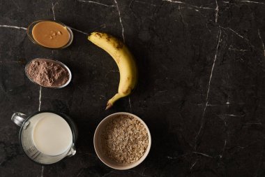 Protein zengini bir Smoothie için gerekenler: Taze muz, rulo yulaf ezmesi, kremalı süt ve çikolatalı protein tozu, sanatsal olarak lüks bir Kara Mermer Yüzeye yerleştirilmiş. Yüksek kalite fotoğraf