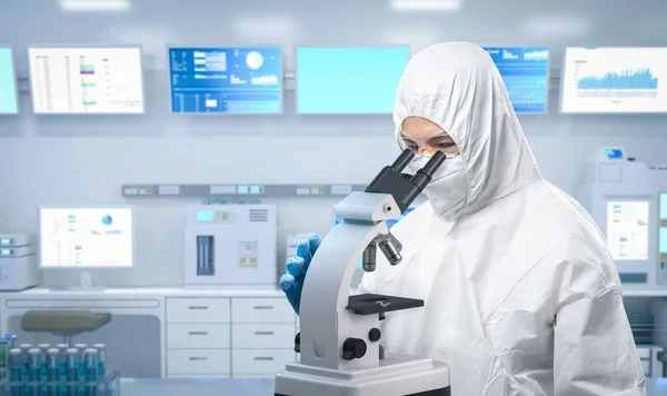 研究室で顕微鏡を通してマスクやゴーグルで医療保護スーツや白いカバースーツを身に着けている労働者 — ストック写真