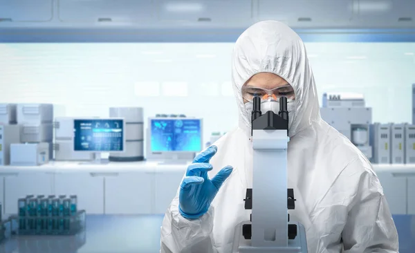 研究室で顕微鏡を通してマスクやゴーグルで医療保護スーツや白いカバースーツを身に着けている労働者 — ストック写真
