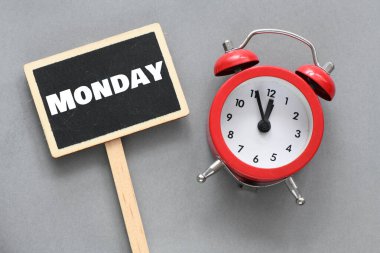 Çalar saatin yanında küçük bir karatahtanın üzerinde Pazartesi kelimesi.