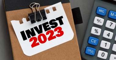 INVEST 2023 kelime bir hesap makinesinin yanında küçük bir kağıt parçası üzerinde.