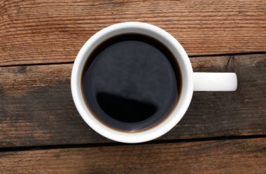 Tahta bir masanın üzerinde kahve olan beyaz bir fincan..