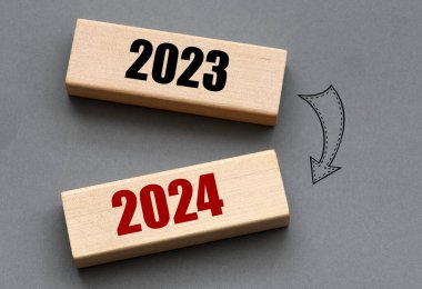 Mutlu Noeller ve 2024 yılına hoş geldiniz. Tahta bloklar ve gri arka planda 2023 ve 2024 tarihleri.