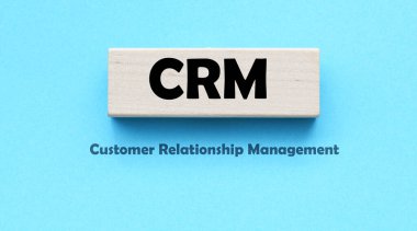 Mavi blok ve mavi arkaplan üzerinde CRM Müşteri İlişkileri Yönetimi sözcükleri.