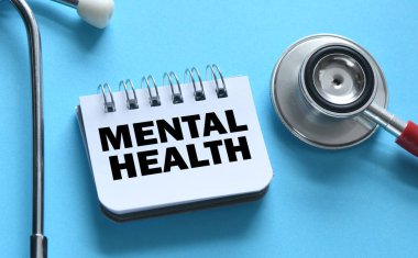 MENTAL Sağlık Sözcükleri bir ofis defterinde steteskopun yanında mavi bir arkaplanda.