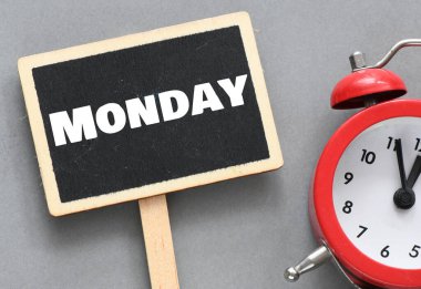 Çalar saatin yanında küçük bir karatahtanın üzerinde Pazartesi kelimesi.