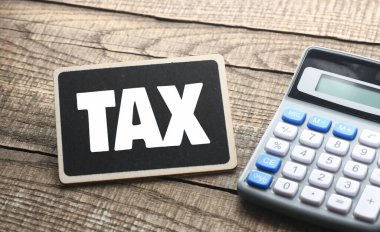 Küçük bir tebeşir tahtasında vergi kelimesi ve hesap makinesinin yanında ahşap bir arkaplan. İş kavramı.