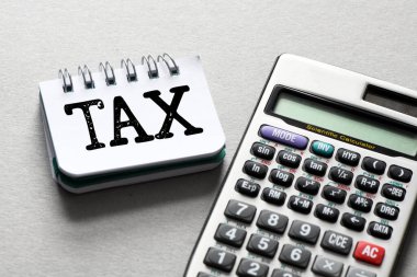 Ofis defterinde, gri bir arkaplanda hesap makinesinin yanında bir vergi kelimesi. Vergi İş Konsepti .