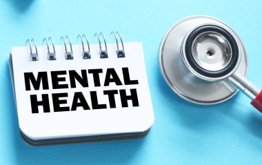 MENTAL Sağlık Sözcükleri bir ofis defterinde steteskopun yanında mavi bir arkaplanda.