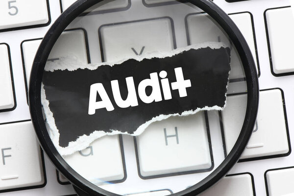 AUDIT word on a black sheet of paper under the magnifying glass.