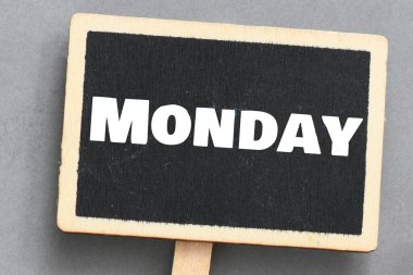 Çalar saatin yanında küçük bir karatahtanın üzerinde Pazartesi kelimesi.