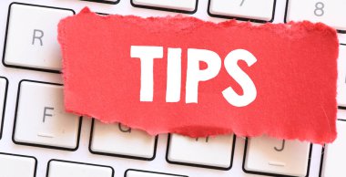 Bilgisayar klavyesinde duran küçük kırmızı bir kağıt parçasındaki TIPS kelimesi.