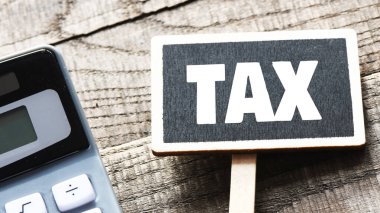 Küçük bir tebeşir tahtasında vergi kelimesi ve hesap makinesinin yanındaki ahşap masa. Vergi İş Konsepti .