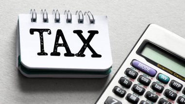 Ofis defterinde, gri bir arkaplanda hesap makinesinin yanında bir vergi kelimesi. Vergi İş Konsepti .