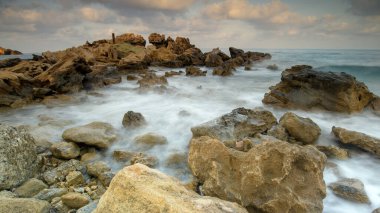 Turkuvaz suları, kumlu bir plaj, kayalık kıyı şeridi ve açık mavi gökyüzü içeren nefes kesici Kıbrıs Akdeniz manzarası. Yaz tatilleri, turizm ve doğa aşıkları için mükemmel bir tatil yeri..