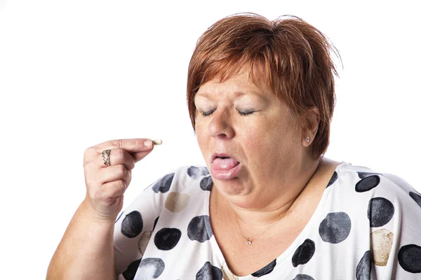 超重的50多岁的女人 一张恶心的脸试图吞下一颗药丸 被白色的背景隔开 免版税图库照片