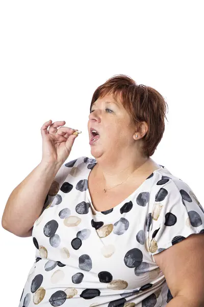 Eine Fünfzigjährige Isst Eine Braune Pille Vor Weißem Hintergrund lizenzfreie Stockbilder