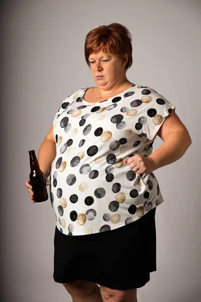 Pięćdziesiąt Coś Tam Kobieta Patrząc Dół Brązową Butelkę Piwa — Zdjęcie stockowe