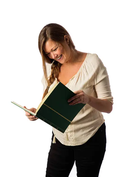 四十来岁的女人 穿着休闲装 阅读一本绿色的大书 在白色的背景下嬉笑着 图库图片