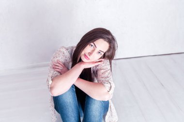 Mütevazı bir kız kolları ve bacakları çaprazlanmış şekilde yerde oturuyor.