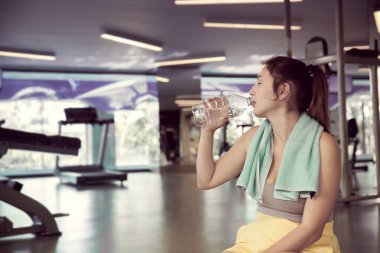Spor salonunda bir kız şişeden su içiyor.
